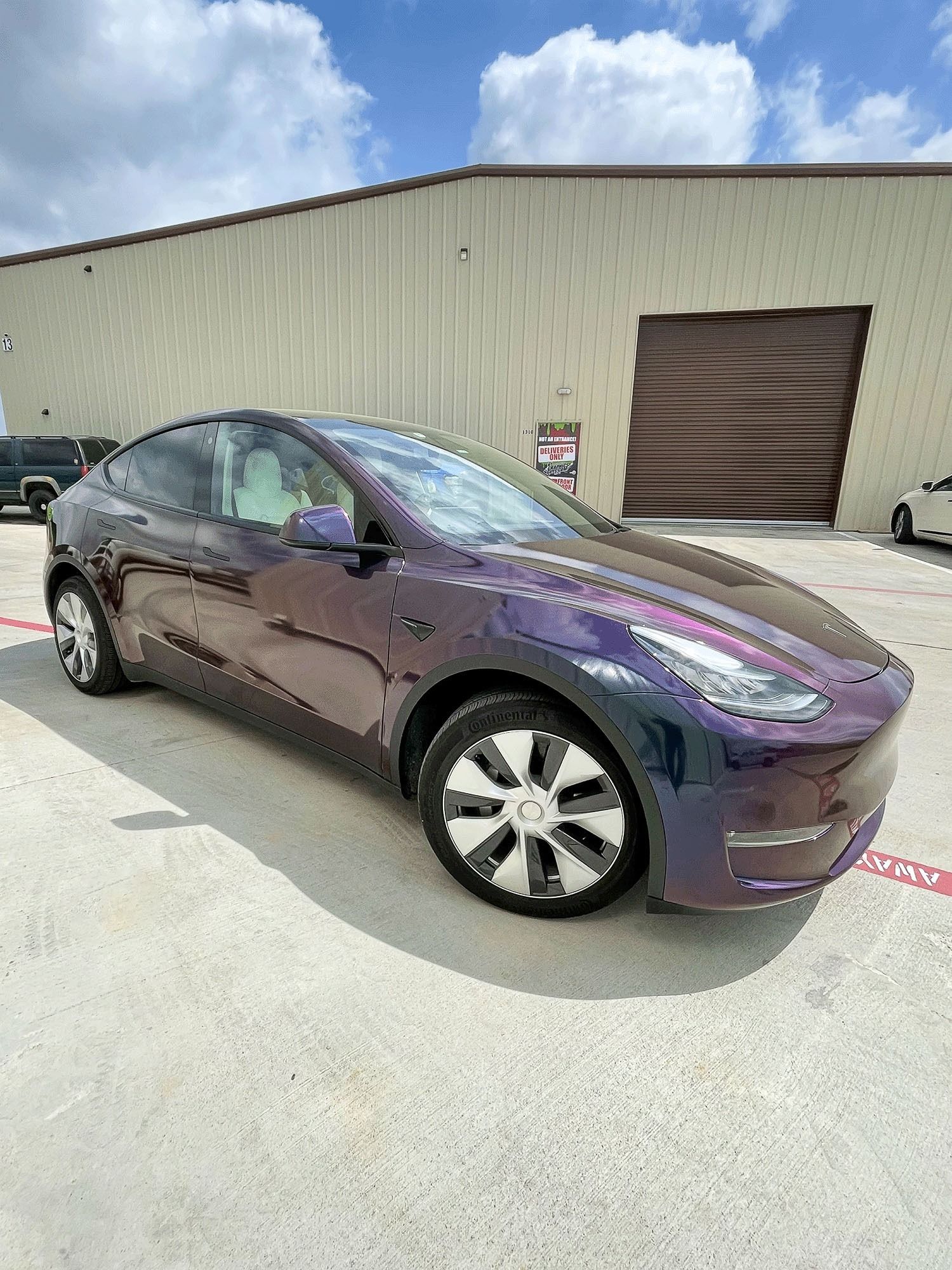 Purple Tesla parked outside an industrial building under a blue sky