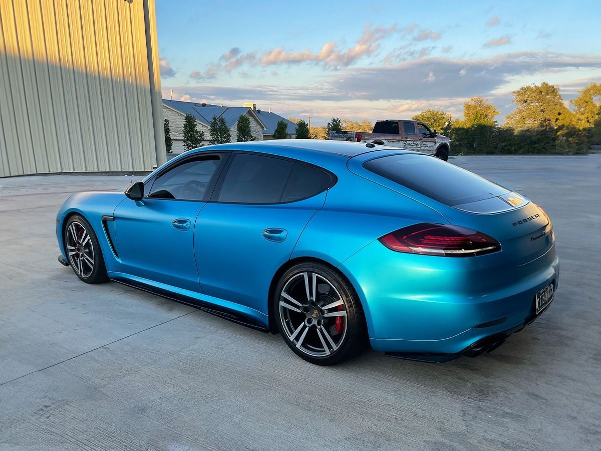 Blue Porsche sedan parked on a concrete lot at sunset
