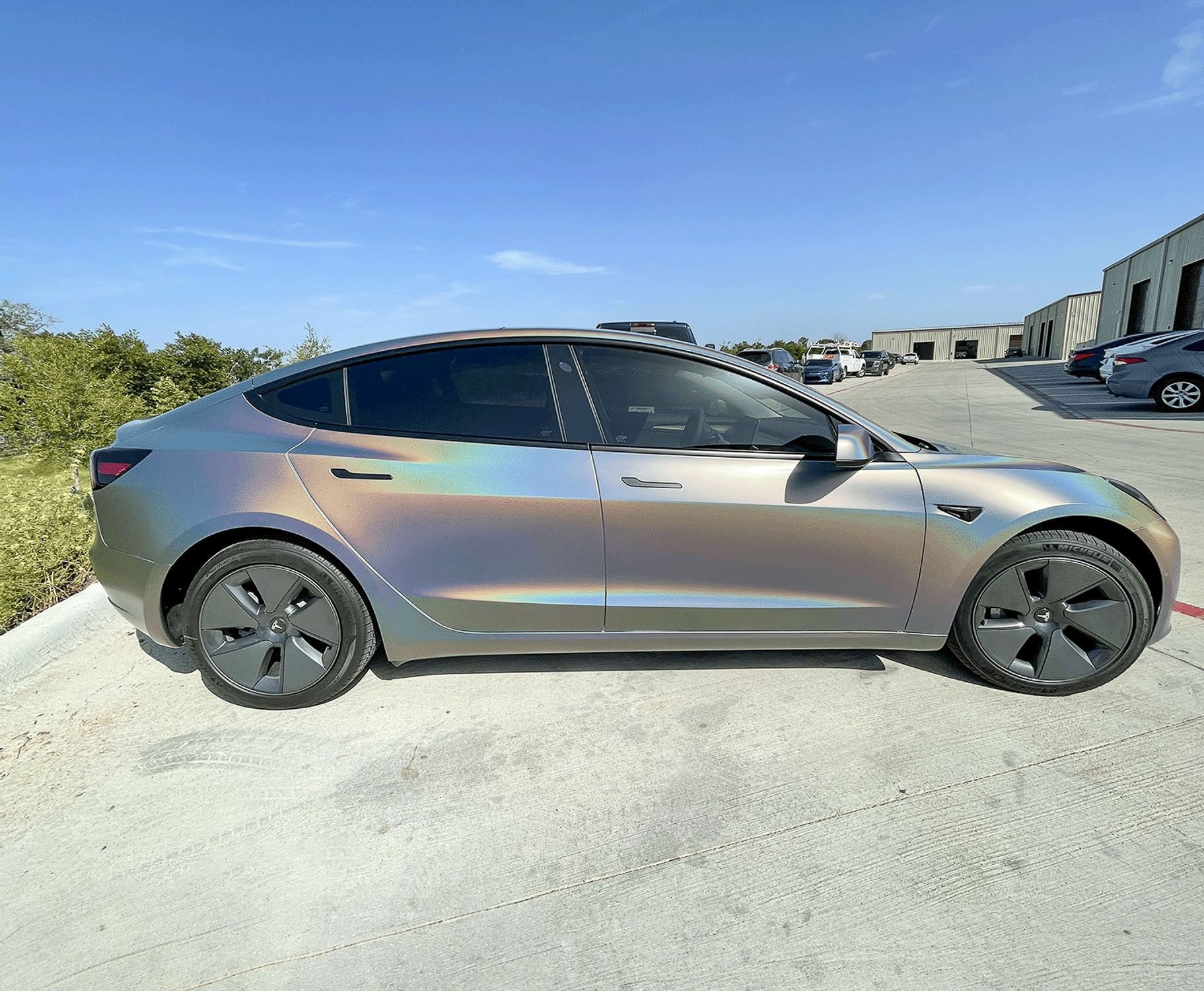 Sleek gray electric sedan parked on a sunlit road beside greenery and a gravel shoulder.