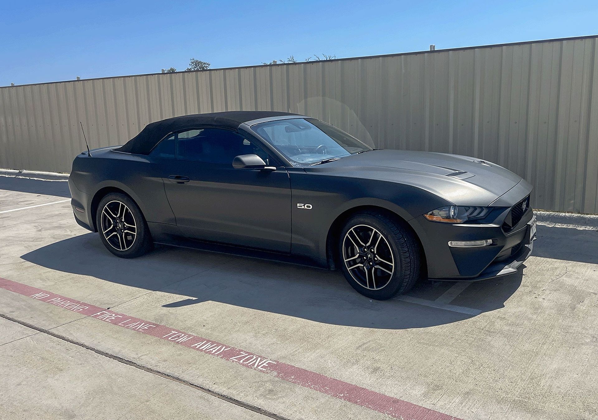 Black sports coupe parked beside a beige wall on a concrete lot