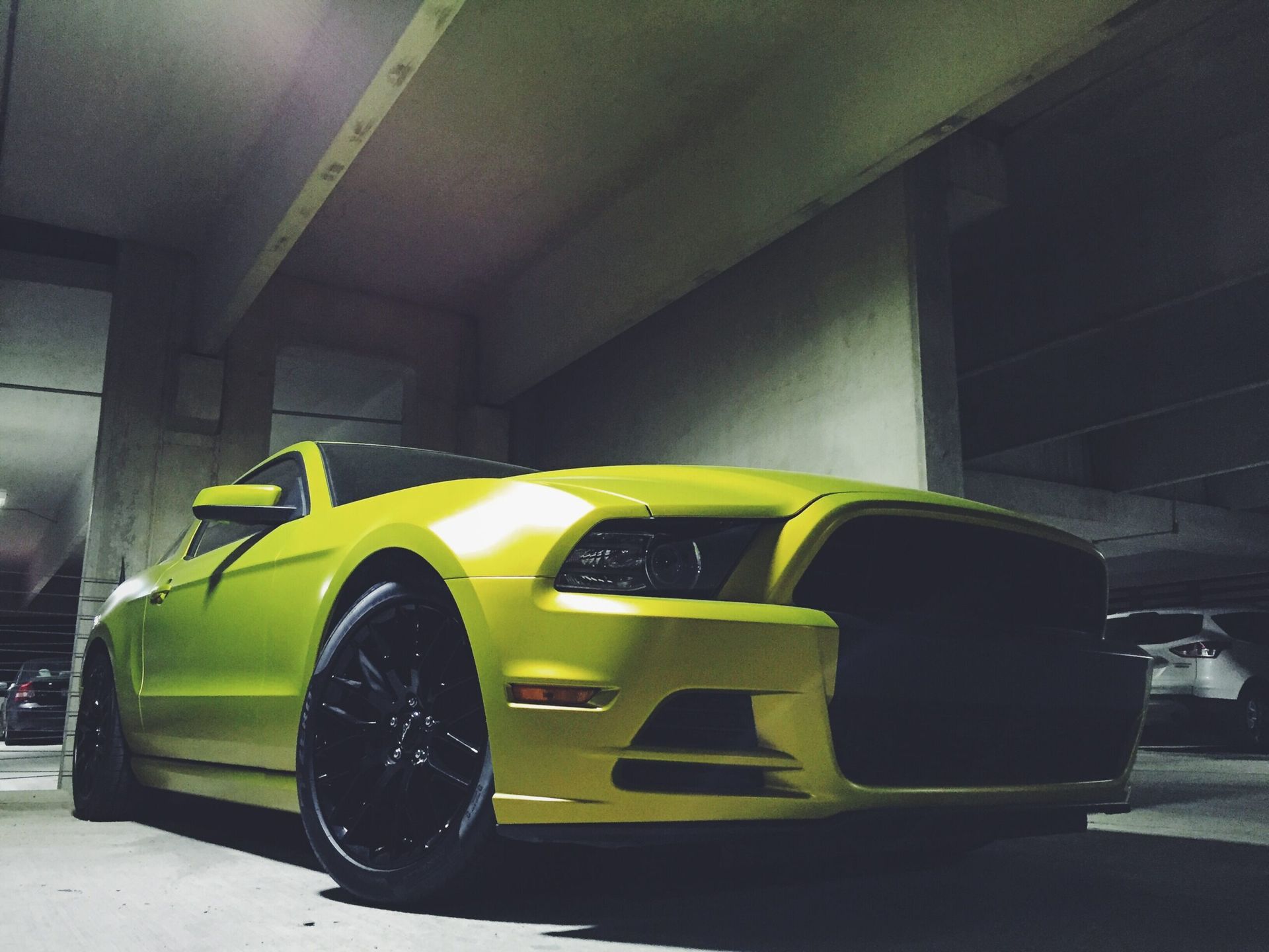 Yellow sports car in a dim concrete parking garage, viewed from the front-left side.