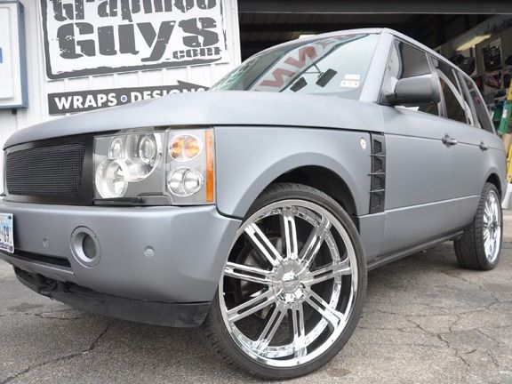 Silver customized sedan with large chrome rims parked in front of a car shop sign.