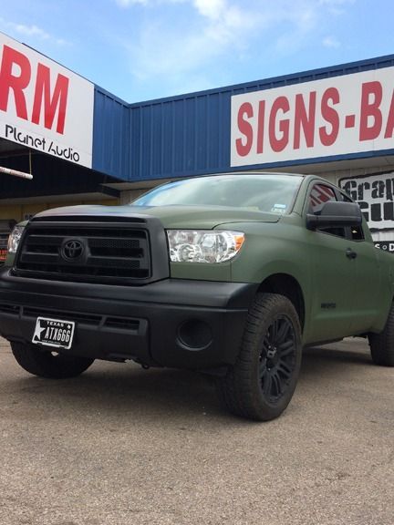 Green Toyota pickup parked in front of a signs store with red-and-white signage.