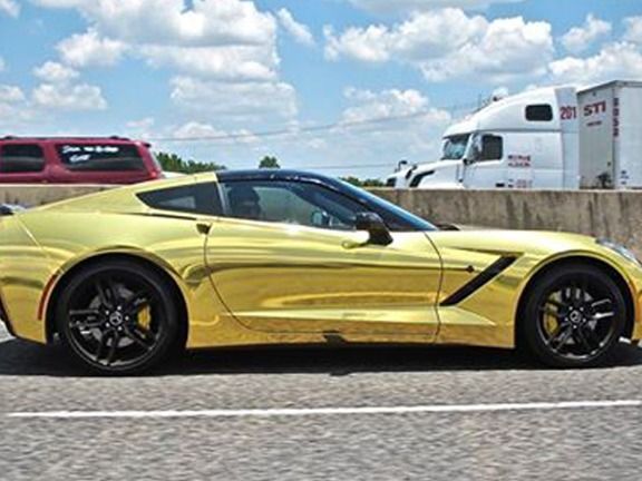 Yellow sports car parked on a road with trucks and cloudy sky in the background