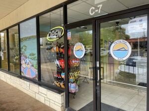 Storefront entrance with glass doors, open sign, and circular logos in a shopping plaza.