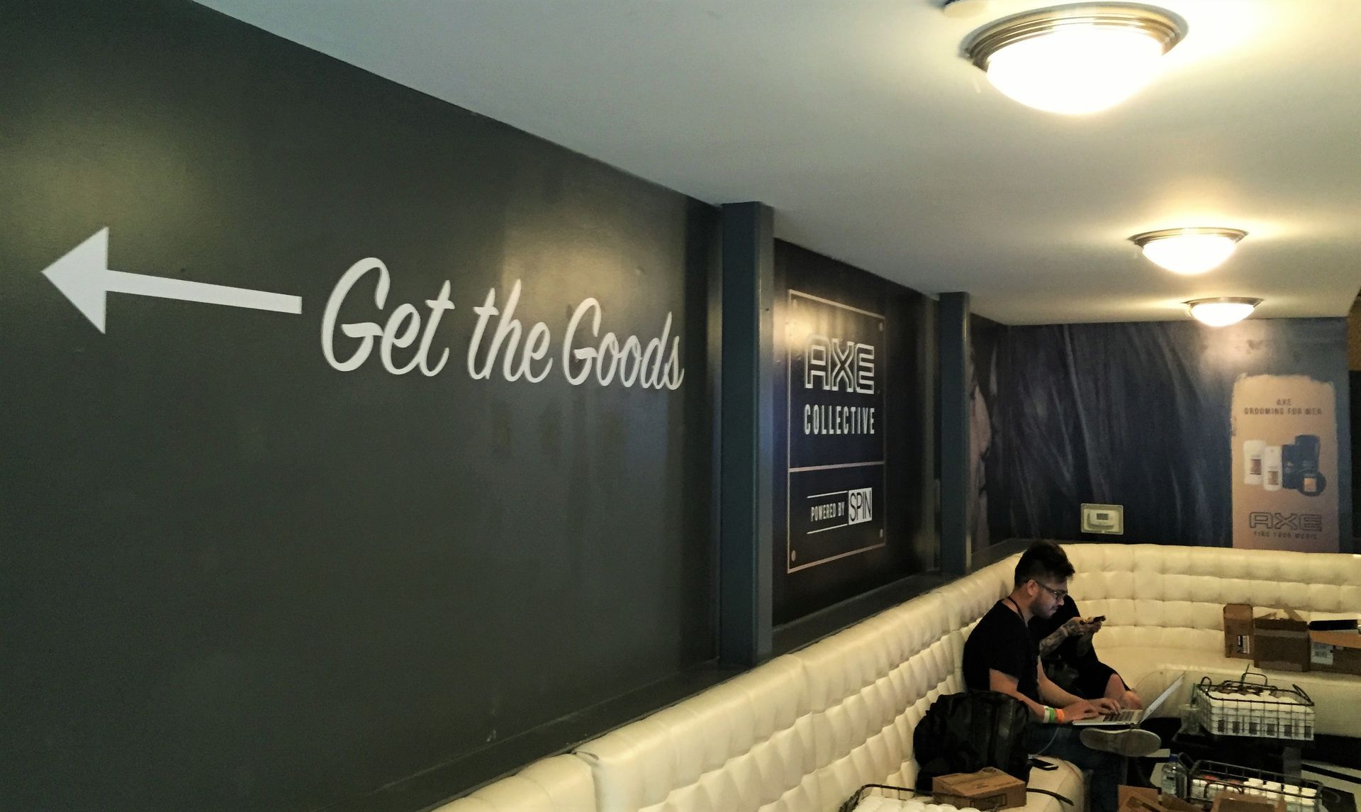 Cafe hallway with “Get the Goods” wall sign and arrow pointing left; a seated person by booths.