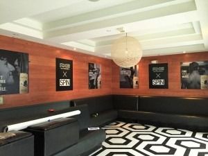 Modern lounge with red walls, black seating, geometric black-and-white floor, and a hanging globe light