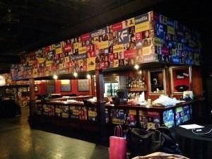 Colorful bar interior with walls covered in logos and a long counter under warm lighting