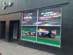 Storefront window poster featuring a race car and the text “Hey Austin, we’re back!”