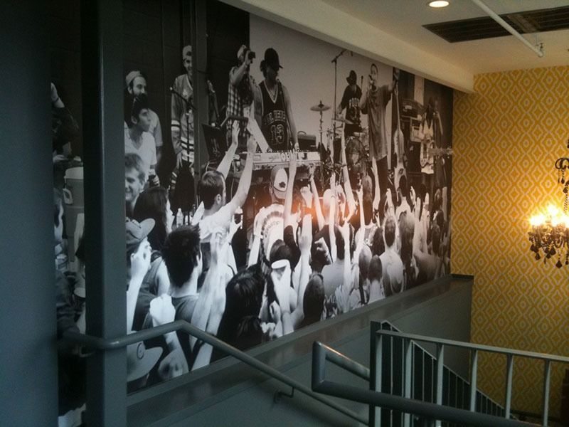 Black-and-white concert mural on a stairwell wall beside a patterned yellow hallway