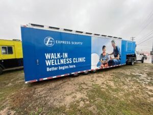 Blue Express Security walk-in wellness clinic trailer in a muddy outdoor lot, with people pictured on the side