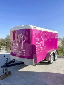 Bright pink enclosed trailer with “The Billar Group” branding parked outdoors on pavement.