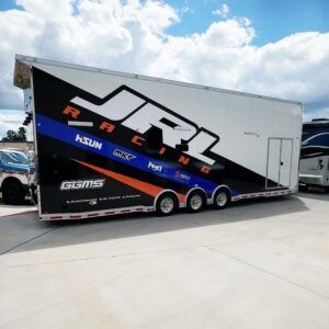 JR1 Racing black and white enclosed trailer with blue accents, parked outdoors on a sunny day
