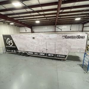 White enclosed car trailer with black branding parked inside a warehouse garage.