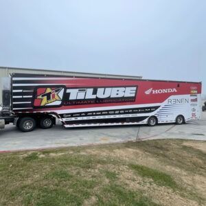 Long black-and-red TILUBE Honda race trailer parked on a gravel lot under a clear sky