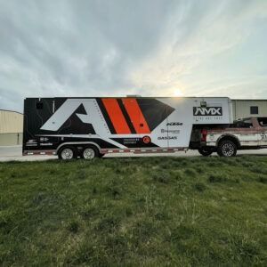 Large black-and-white trailer with orange accents parked on grass at sunset