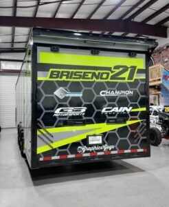 Trailer with bright green BRISENO 21 racing graphics in a garage workshop