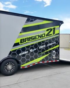 Black trailer with neon green Brisend 21 racing graphics parked on pavement.