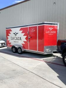 White LA CAZA trailer with red and white branding parked beside a gray industrial building.