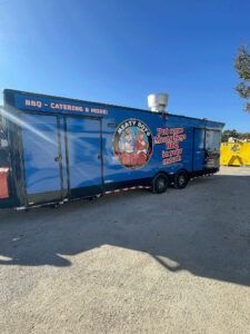 Blue catering trailer parked outdoors in a lot, with red lettering and a large logo on the side.