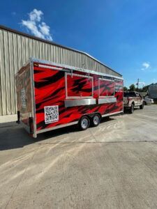 Red and black enclosed trailer parked beside a warehouse on a sunny day
