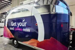 Blue and pink trailer with “Get your next home now” branding inside a showroom