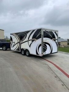 Black-and-white enclosed trailer parked on a concrete lot near buildings