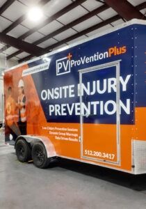 Orange and blue trailer with “Onsite Injury Prevention” branding parked inside a warehouse