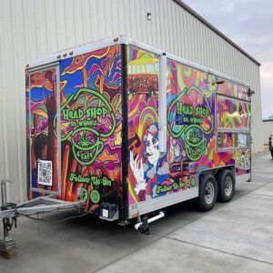 Graffiti-covered food trailer parked on concrete, with colorful psychedelic art and a hitch at the front.