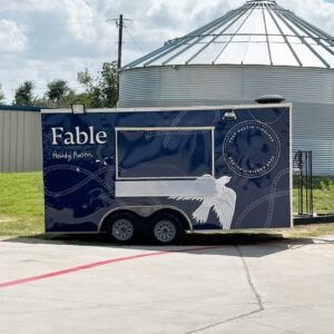 Blue Fable mobile trailer with white bird graphic parked outdoors near a silo