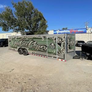 Custom-painted vintage trailer with ornate green script parked on a sunny dirt lot