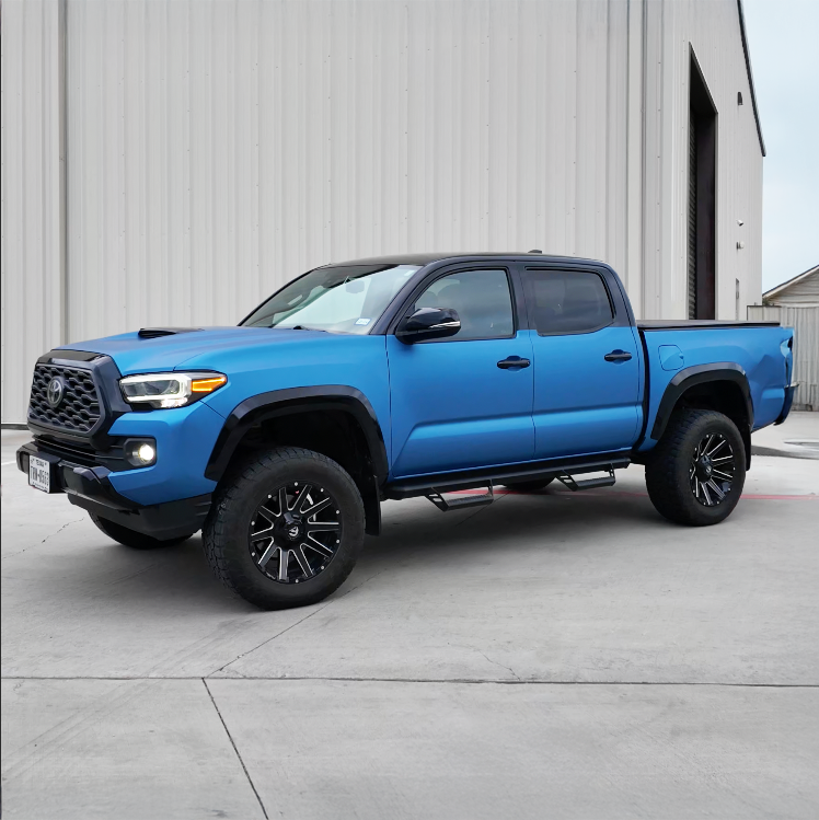 Blue pickup truck parked beside a gray building on a concrete lot