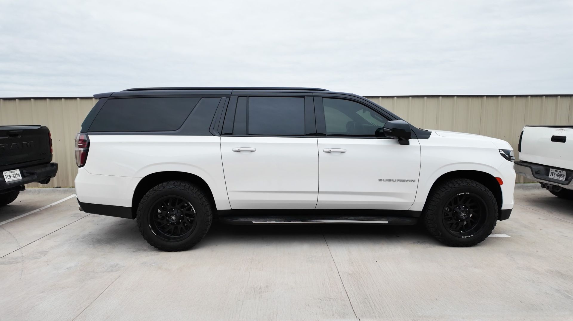 White SUV with black roof and wheels parked on a concrete lot against a fence.