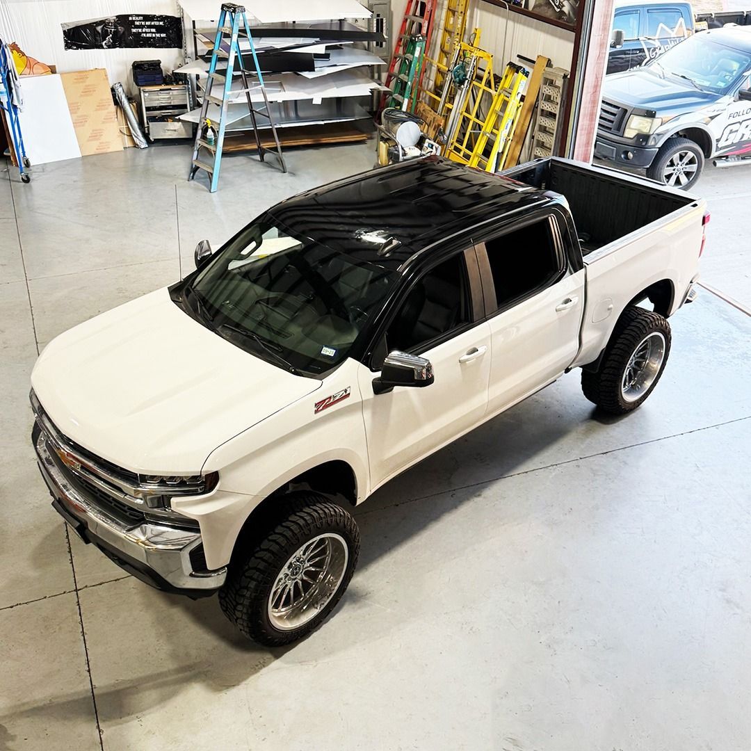 White and black lifted pickup truck in a garage with tools and equipment in the background