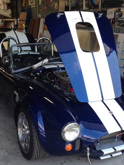 Blue vintage sports car with white racing stripes and open hood in a garage