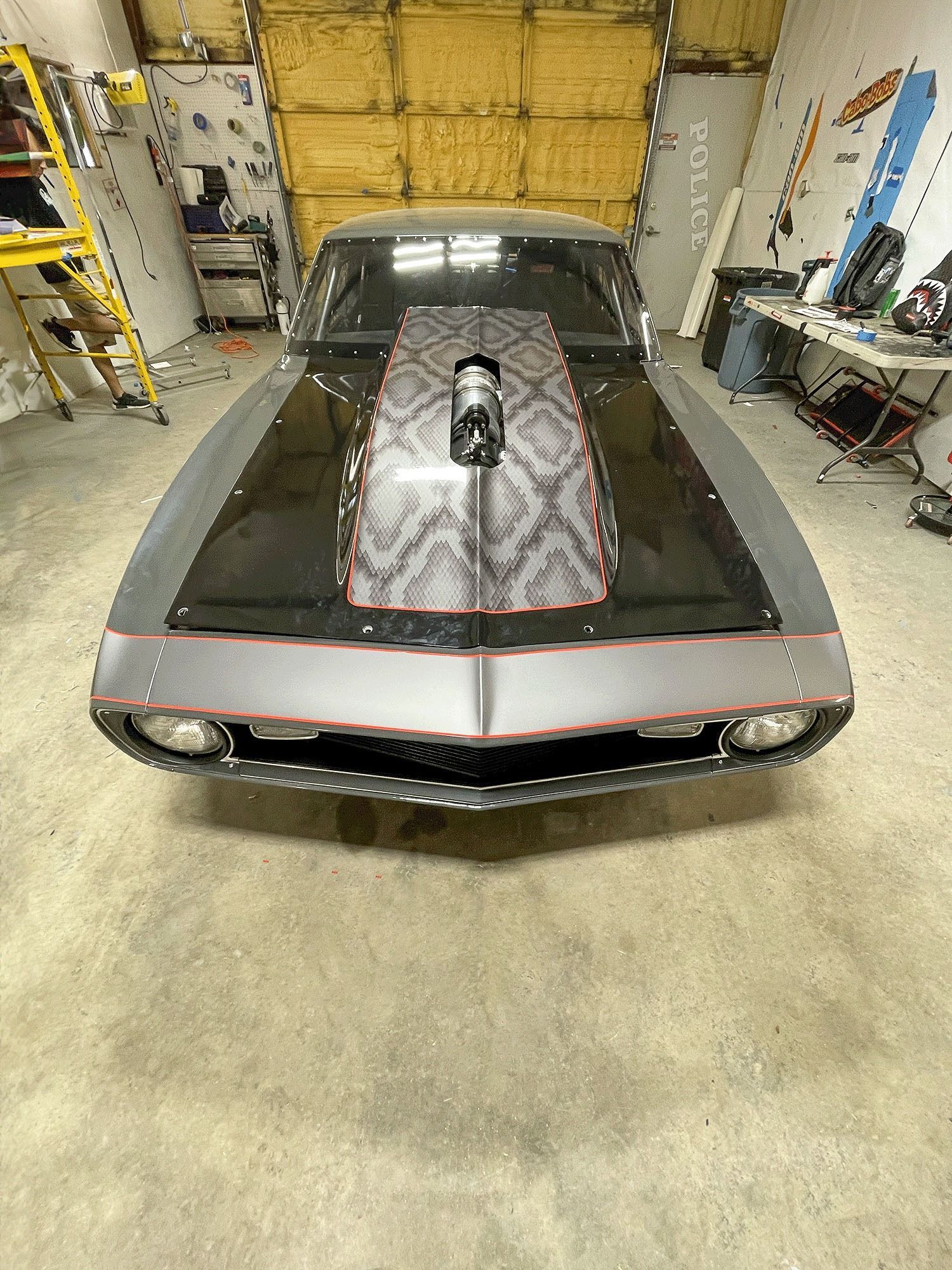 Classic car in a garage, front view with hood open and engine exposed.