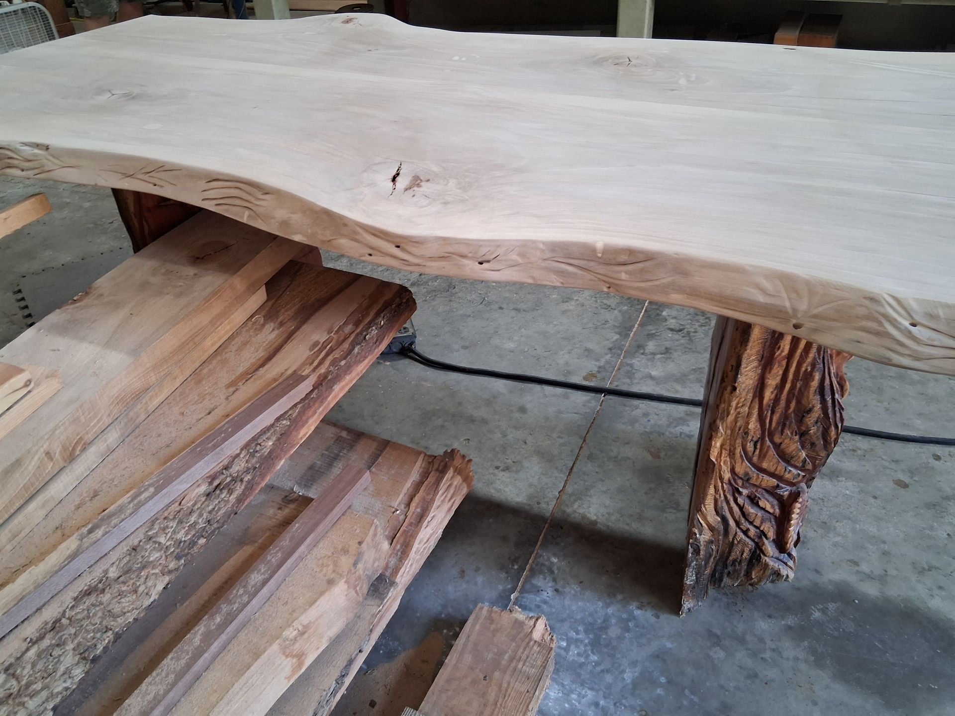 Wooden bench with a live-edge table and rustic tree-trunk legs on a concrete floor
