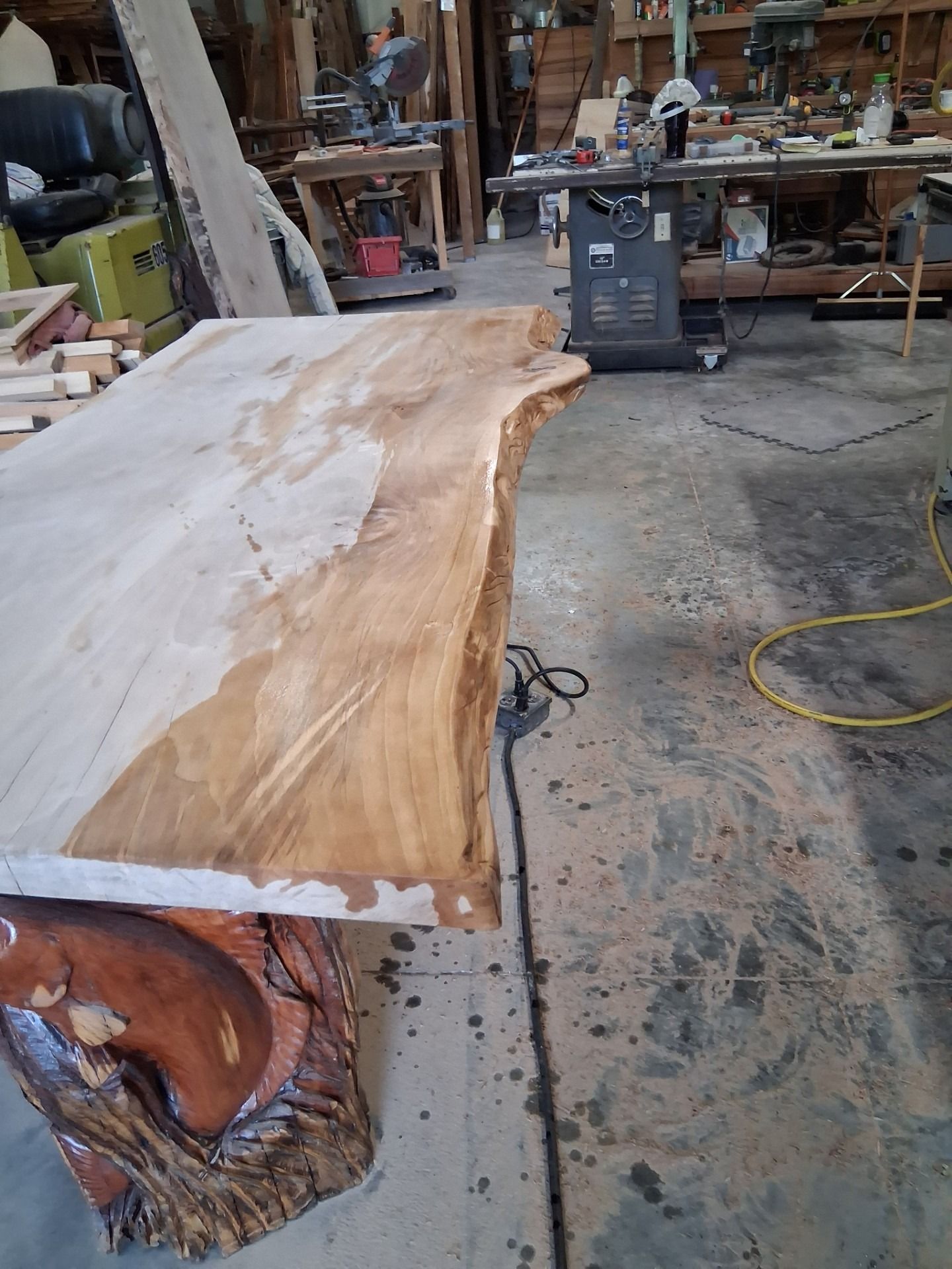 Live-edge wooden slab on workshop floor with tools and sawdust nearby