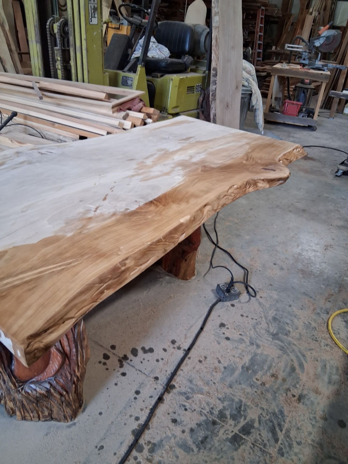 Live-edge wooden table in a workshop with tools and lumber in the background