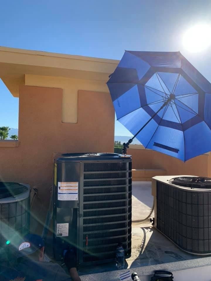 Blue umbrella shading a rooftop air conditioning unit in bright sunlight.