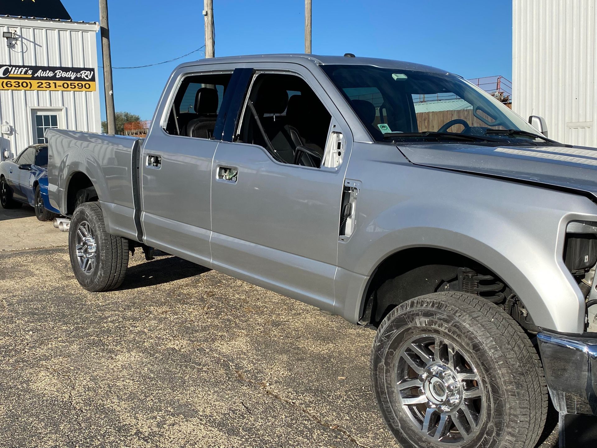 a silver pickup truck is parked in a gravel lot in front of a building