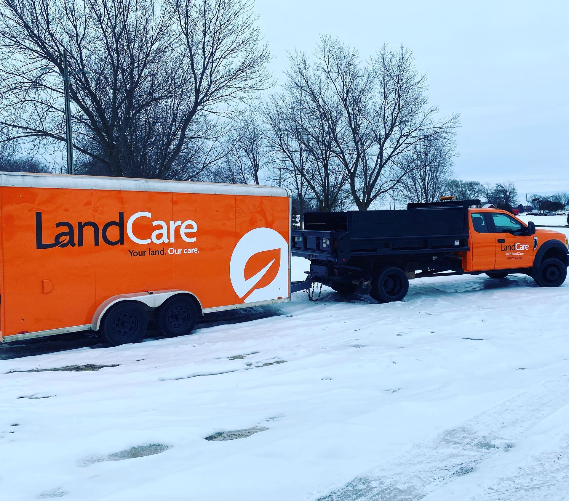 an orange landcare truck is pulling a trailer in the snow