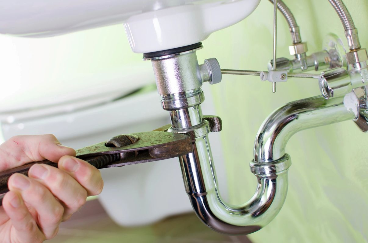 Person using a wrench to tighten plumbing under a white sink.