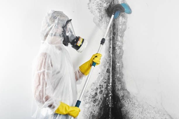 A person in a protective suit is cleaning a wall with a broom.