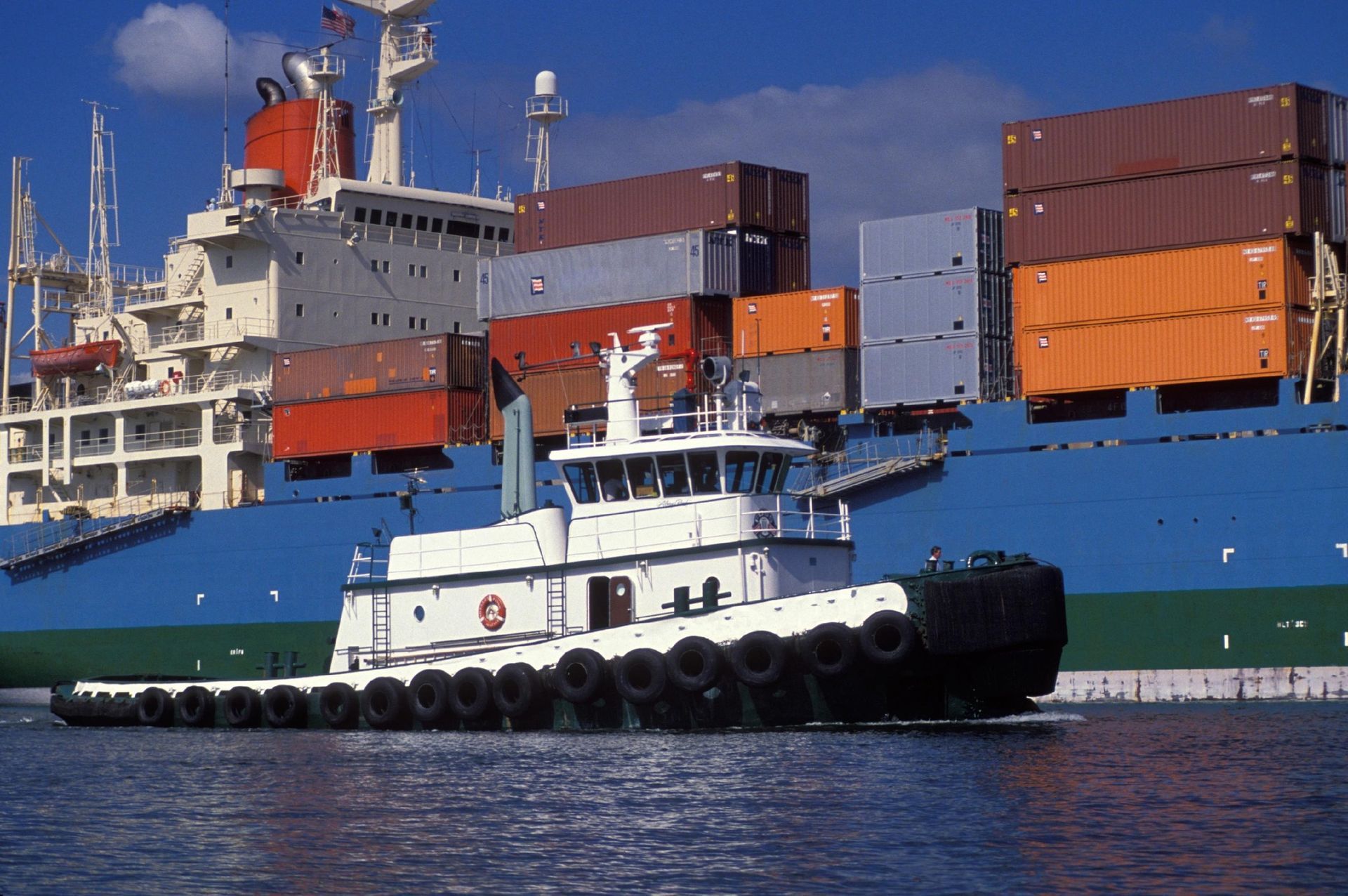 A tugboat in front of a large container ship