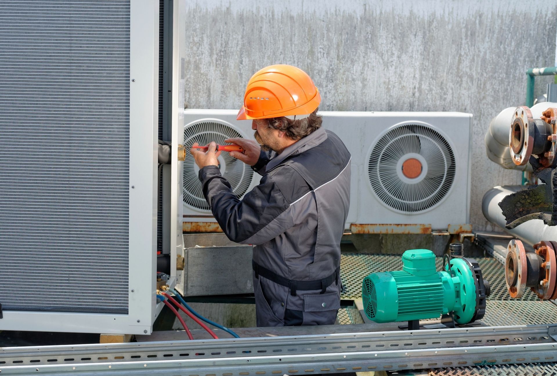 A man wearing an orange hard hat is working on an air conditioner.