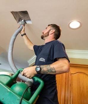 A man is using a vacuum cleaner to clean a hole in the ceiling