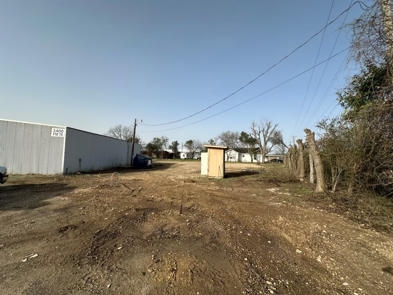 A dirt road with a building in the background and a fence in the foreground.