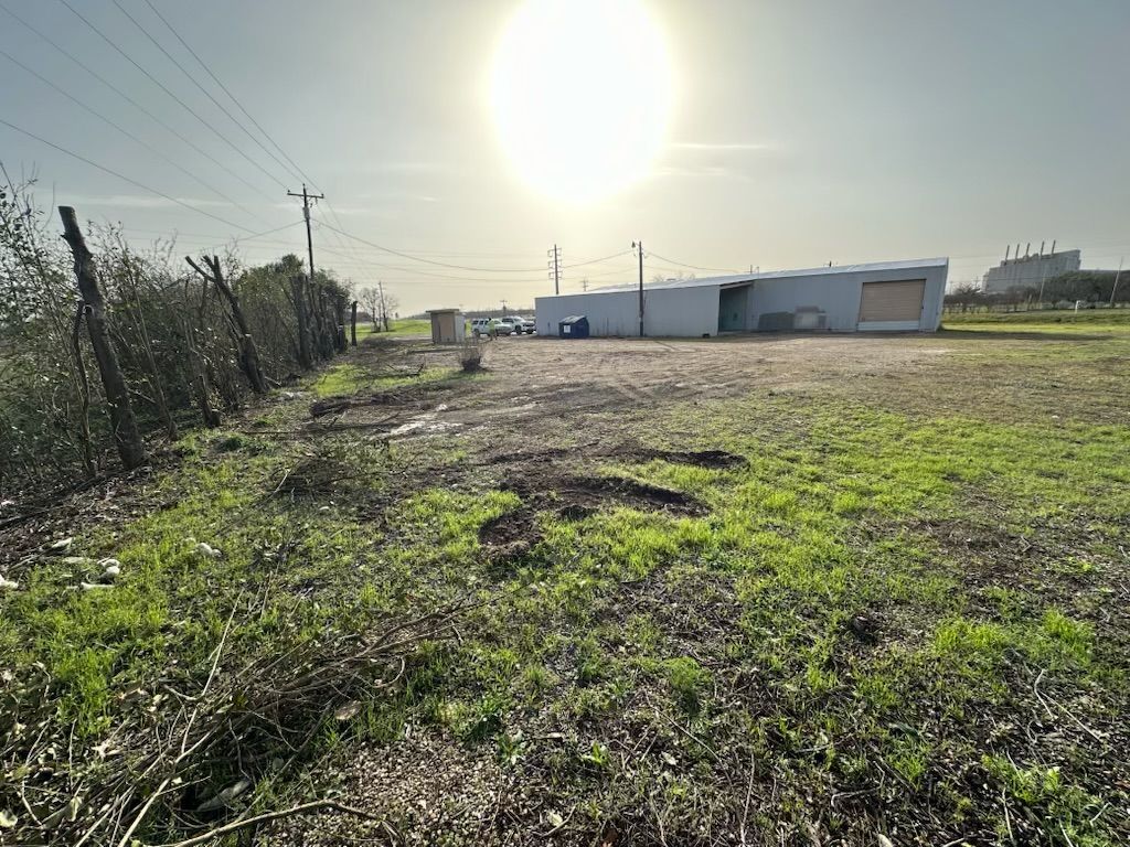 A large grassy field with a fence and a building in the background.