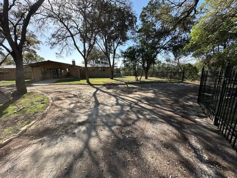 A dirt road leading to a house with trees in the background.